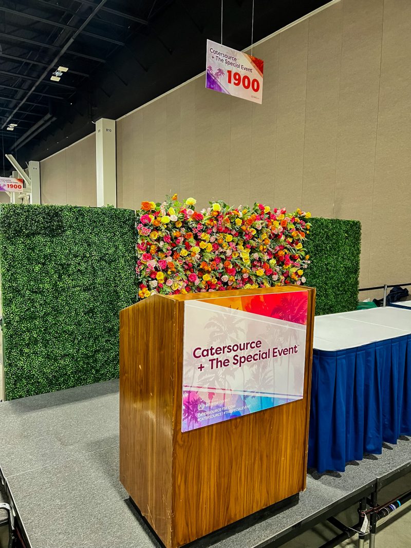 a catersource podium with flower wall backdrop and hedge wall behind it