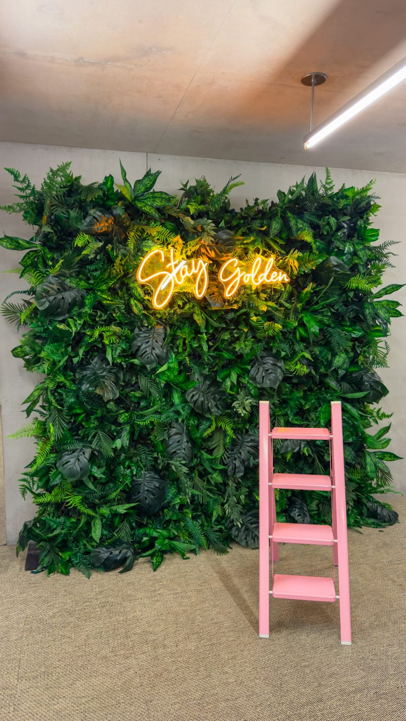 a tropical green wall with a pink ladder and a neon sign