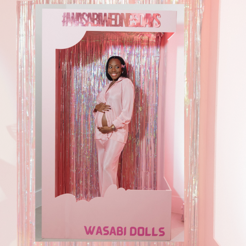 a pregnant woman in a pink garment in a barbie box photo-op