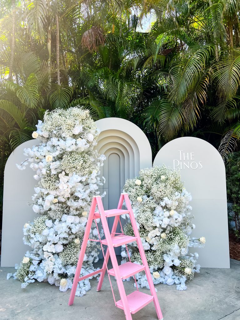 a pink ladder next to a white stone wall with flowers